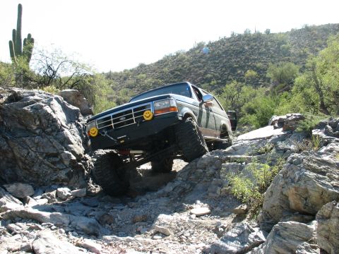 1994 Ford Bronco - A modified Ford Bronco tackles a challenging rocky terrain in a desert landscape.
