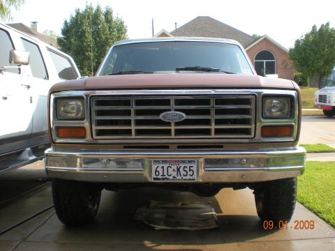 1986 Ford Bronco - Front view of a 1986 Ford Bronco with a chrome grille and bumper, parked next to another vehicle.