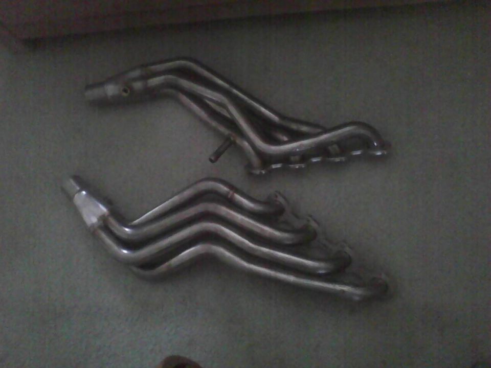 Two chrome exhaust headers on a dark surface, one above the other