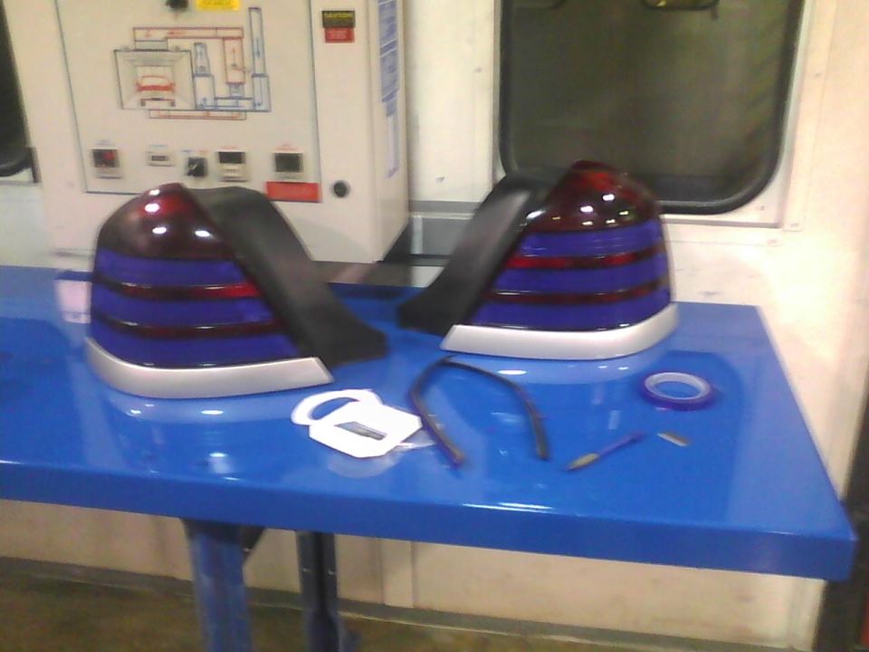 Two aftermarket tail lights with blue and red lenses and silver trim sit on a blue table next to some installation supplies