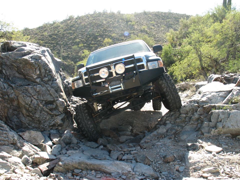 Lifted black Ford truck with winch bumper crawling over rocks in the desert
