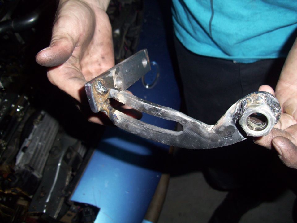 Hands holding a welded metal bracket with a bolt hole