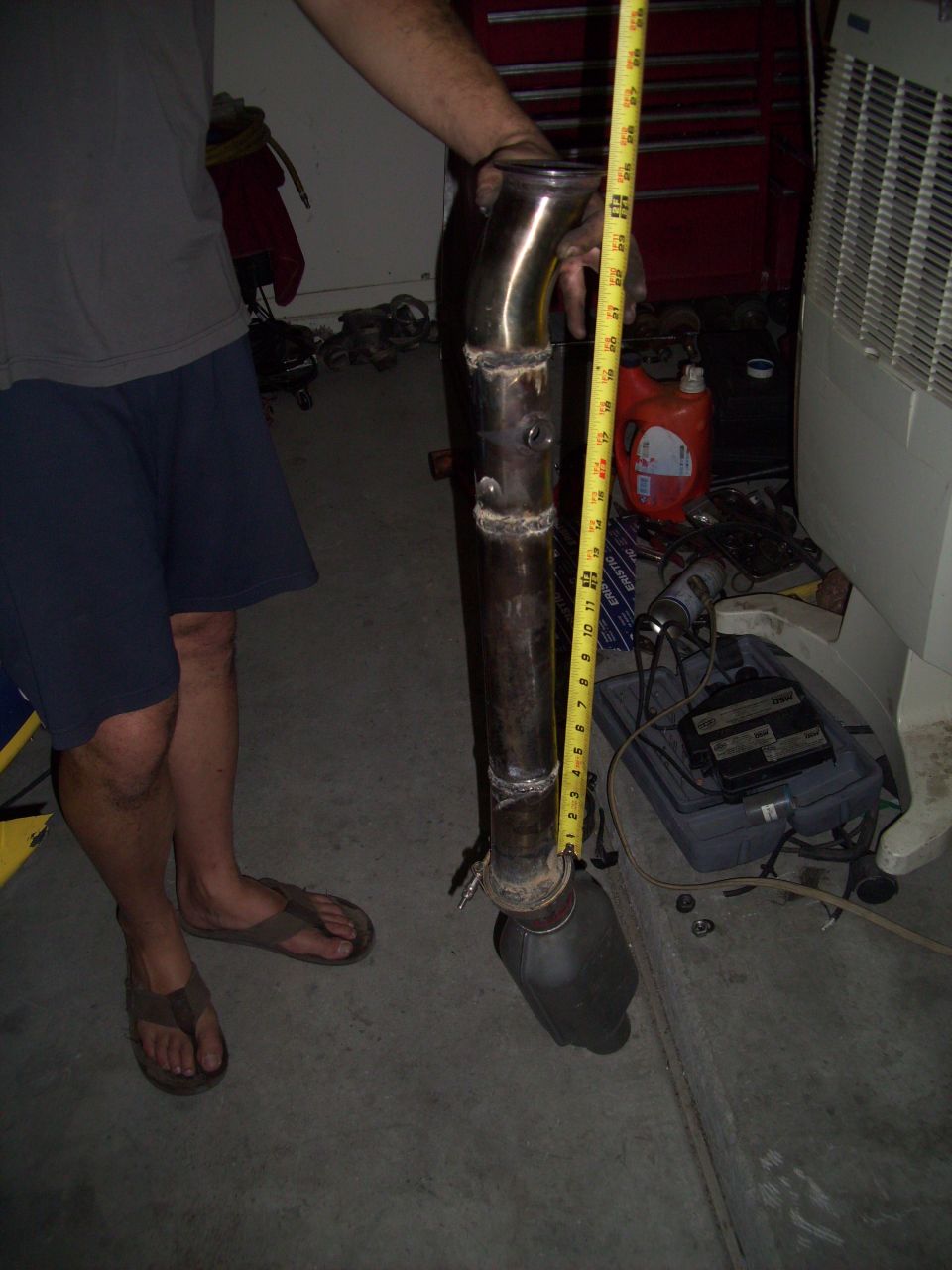 Exhaust pipe with catalytic converter being measured with a tape measure