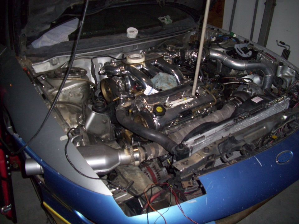Engine bay of a car with a chrome intake manifold and various hoses and wires visible