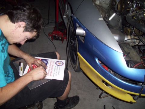 1995 Ford Probe - A person is working on the front of a vehicle, holding a document with text and a seal.