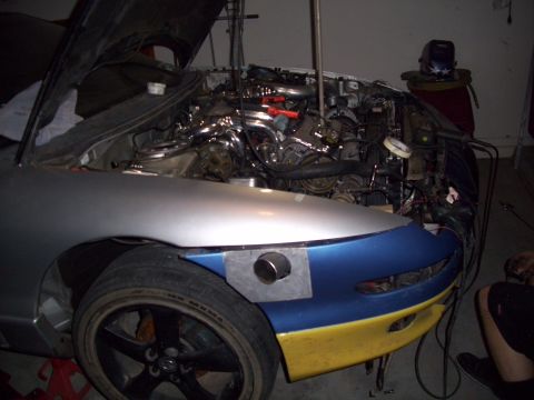 1995 Ford Probe - The engine bay of a car is visible with the hood up, and the front bumper is painted blue and yellow.