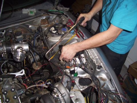 1995 Ford Probe - A person works on the engine bay of a car, using a hacksaw amidst a tangle of wires and engine components.