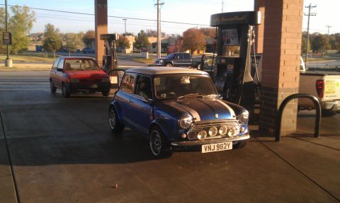 1991 Ford Festiva - A blue Mini Cooper is parked at a gas pump, with a red car visible behind it.