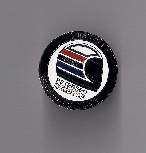 Circular badge with a racing helmet graphic and text reading "TRIBUTE TO GEORGE FOLLMER PETERSEN AUTOMOTIVE MUSEUM NOVEMBER 8, 2012"