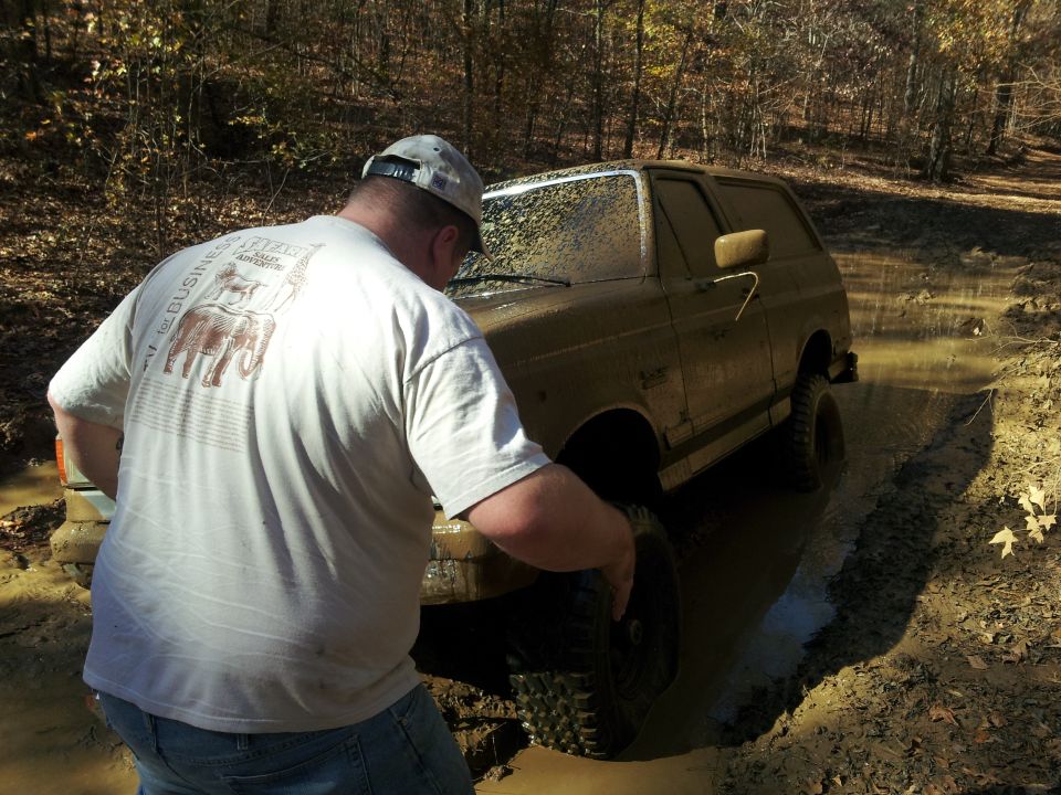 Muddy 1986 Ford Bronco stuck in a ditch, driver checking wheel