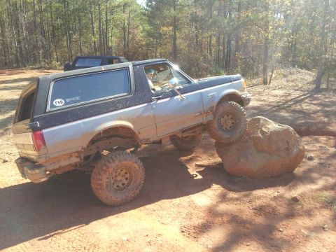 1986 Ford Bronco - This lifted Bronco is navigating a challenging off-road obstacle course in a wooded area.