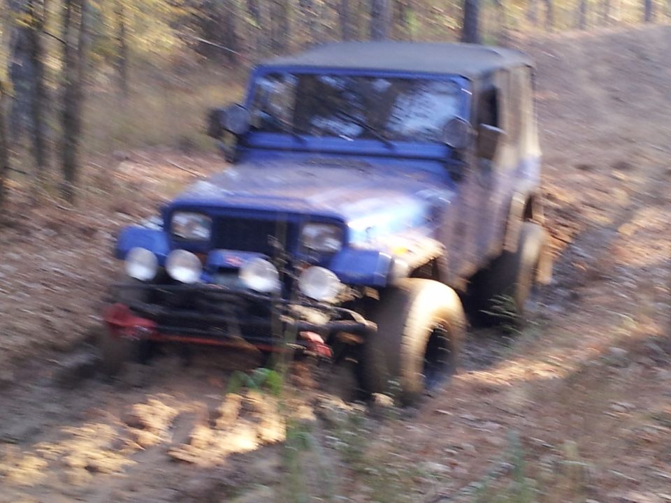 Blue Jeep Wrangler with off-road tires and winch on a dirt path