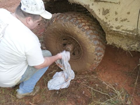 1986 Ford Bronco - Man cleaning mud off a large off-road tire.