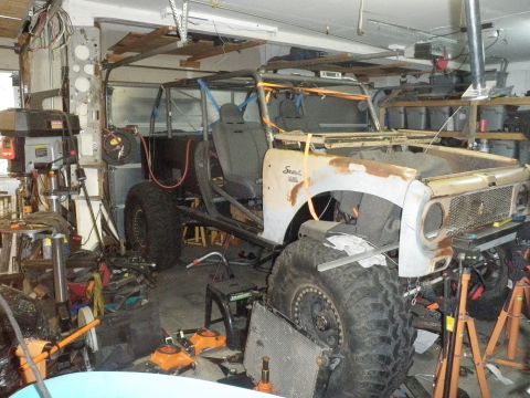 1961 International Scout 800 - This vehicle is in a garage, appearing to be undergoing modifications or repairs, with a custom roll cage and oversized tires.
