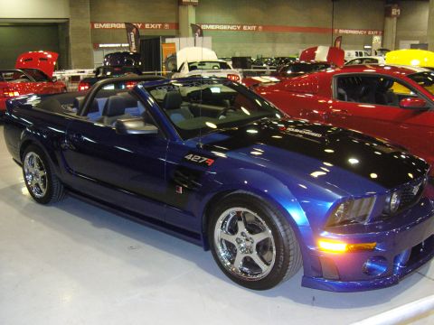 2007 Ford Mustang - A blue convertible sports car is displayed indoors, with other vehicles around it.