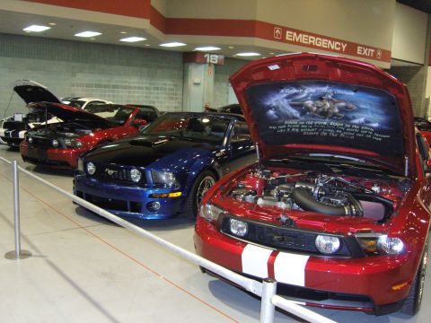 2007 Ford Mustang - A red 2007 Ford Mustang is displayed with its hood open, revealing custom artwork and text. Other Mustangs are visible in the background.