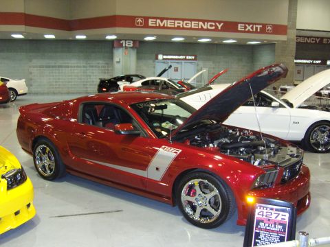 2007 Ford Mustang - A red Ford Mustang with its hood open is displayed alongside other vehicles at an indoor event.