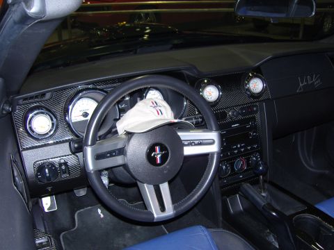 2007 Ford Mustang - The interior of a car shows a dashboard with carbon fiber accents and a baseball cap on the steering wheel.