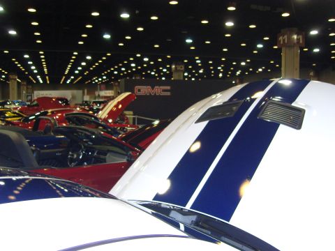 2007 Ford Mustang - Indoor car show with various vehicles on display, some with hoods open and racing stripes.