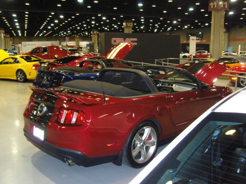 2007 Ford Mustang - A red convertible is parked indoors with its hood open, alongside other vehicles.