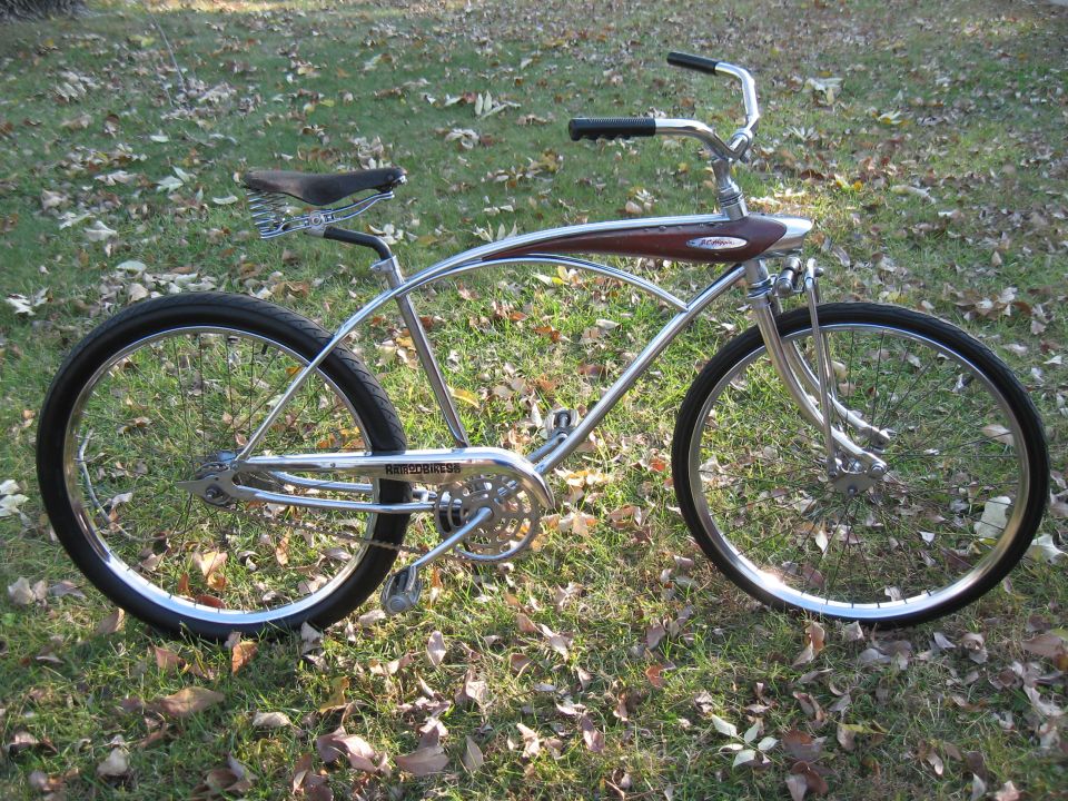 Chrome cruiser bike with brown tank and spring seat, parked on grass with fallen leaves