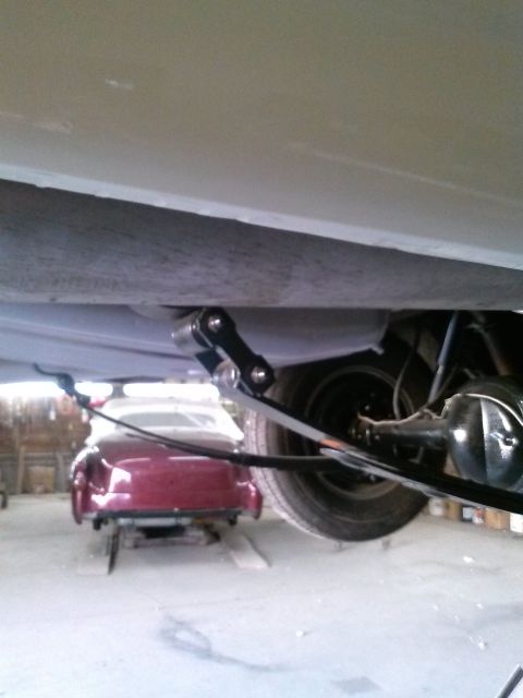 1960 Ford Falcon - Underside view of a vehicle's rear suspension system, with a vintage red coupe in the background.