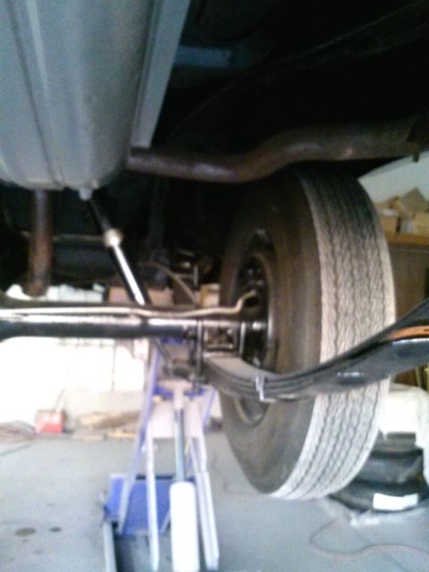1960 Ford Falcon - The rear suspension and exhaust system of a vehicle are visible, supported by jack stands in a garage.
