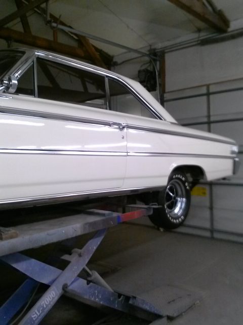 1960 Ford Falcon - Side view of a white sedan being serviced on a lift, chrome trim and a visible tire.