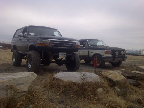 1995 Ford Bronco - Two trucks, a black Bronco and a white and black pickup, are parked outdoors on a cloudy day near large rocks.