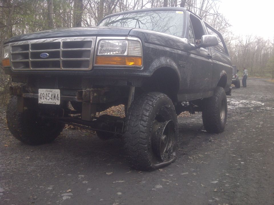 Black 1995 Ford Bronco with a flat tire on a dirt road