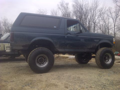 1995 Ford Bronco - Side view of a lifted 1995 Ford Bronco with large tires, parked outdoors.