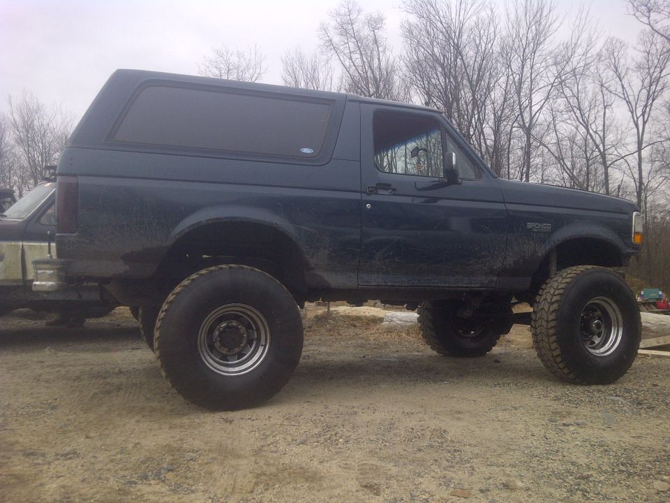 Lifted dark green 1995 Ford Bronco parked on dirt, another vehicle partially visible to the left