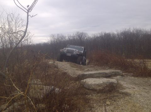 1995 Ford Bronco - A Jeep Wrangler navigates a rocky obstacle course under an overcast sky.