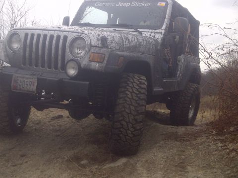 1995 Ford Bronco - A muddy Jeep Wrangler with off-road tires navigates an uneven dirt path.