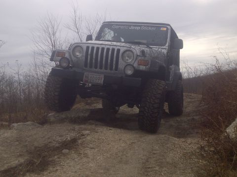 1995 Ford Bronco - A silver Jeep Wrangler navigates a challenging rocky trail with its front-left tire off the ground.