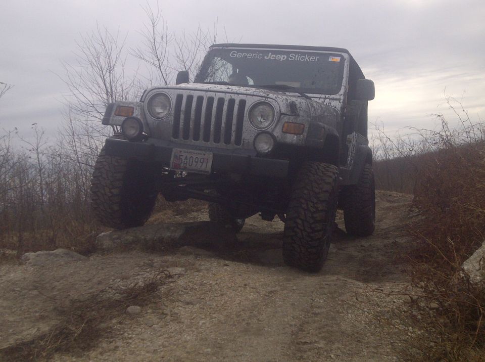 Silver Jeep Wrangler on rocky terrain, front-left tire lifted