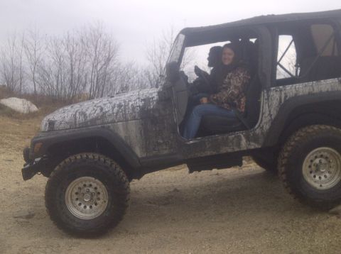 1995 Ford Bronco - Two people sit inside a muddy Jeep Wrangler on an overcast day.