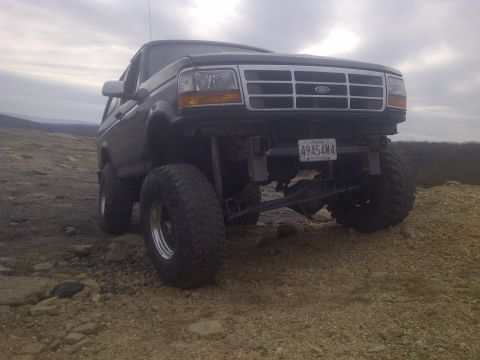 1995 Ford Bronco - This lifted Ford Bronco is parked on a rocky, uneven surface under an overcast sky.