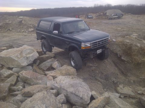 1995 Ford Bronco - A dark blue Ford Bronco navigates a challenging rocky off-road course.