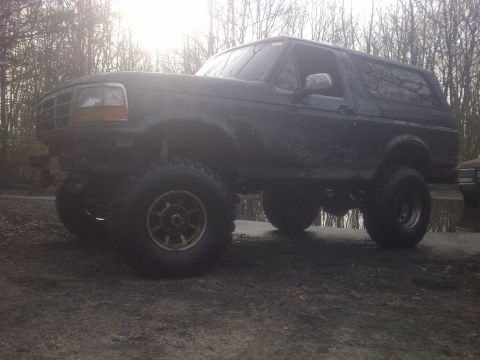 1995 Ford Bronco - A dark-colored, lifted 1995 Ford Bronco sits on a muddy, wooded trail.