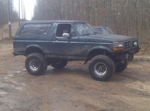 1995 Ford Bronco - Muddy 1995 Ford Bronco on a dirt road, with another vehicle partially visible behind it.