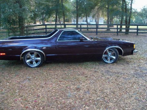 1979 Ford Ranchero - Driver-side profile of a lowered dark maroon Ford coupe-utility with a glossy custom paint job, chrome window and wheel-arch trim, and larg…