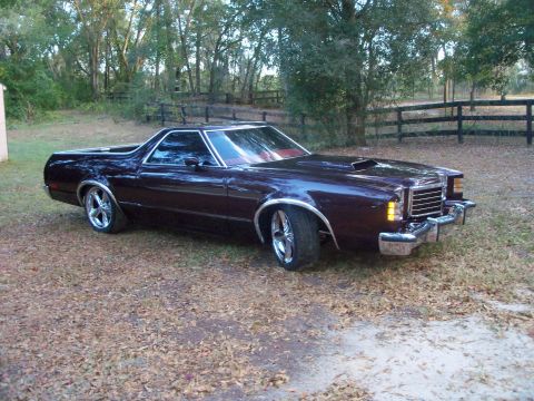 1979 Ford Ranchero - Three-quarter front view of a deep burgundy coupe-utility with a high-gloss finish parked on grass beside a black board fence and oak trees…