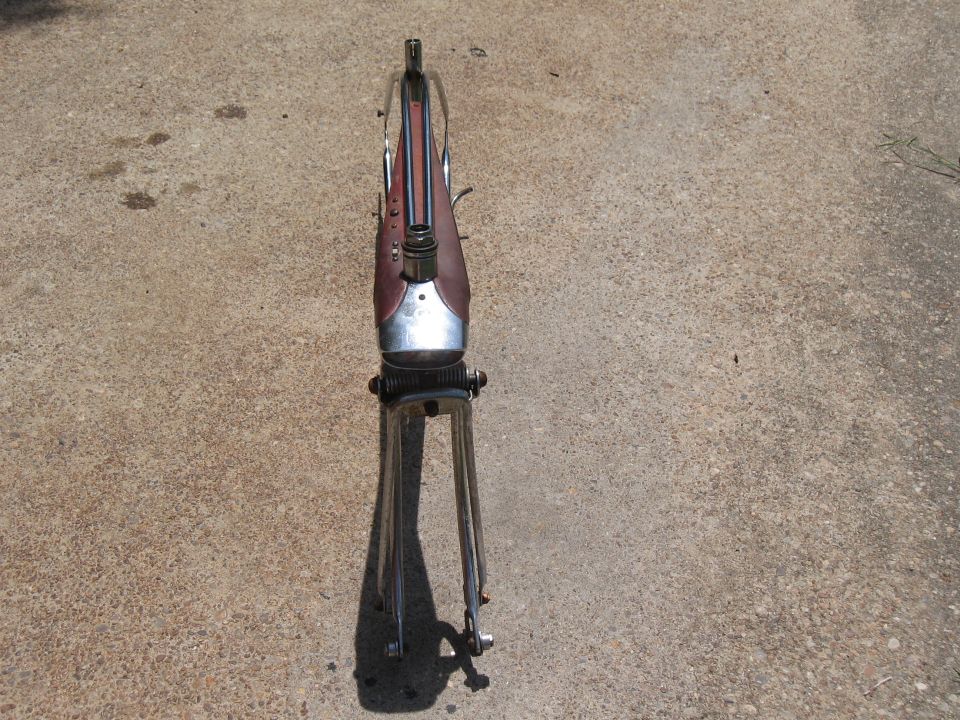 Motorcycle frame with a maroon tank and chrome front forks, resting on concrete