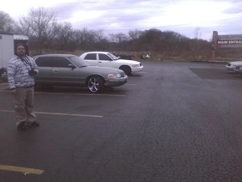 2003 Ford Crown Victoria - A gray 2003 Ford Crown Victoria is parked in a lot next to a white Crown Victoria.