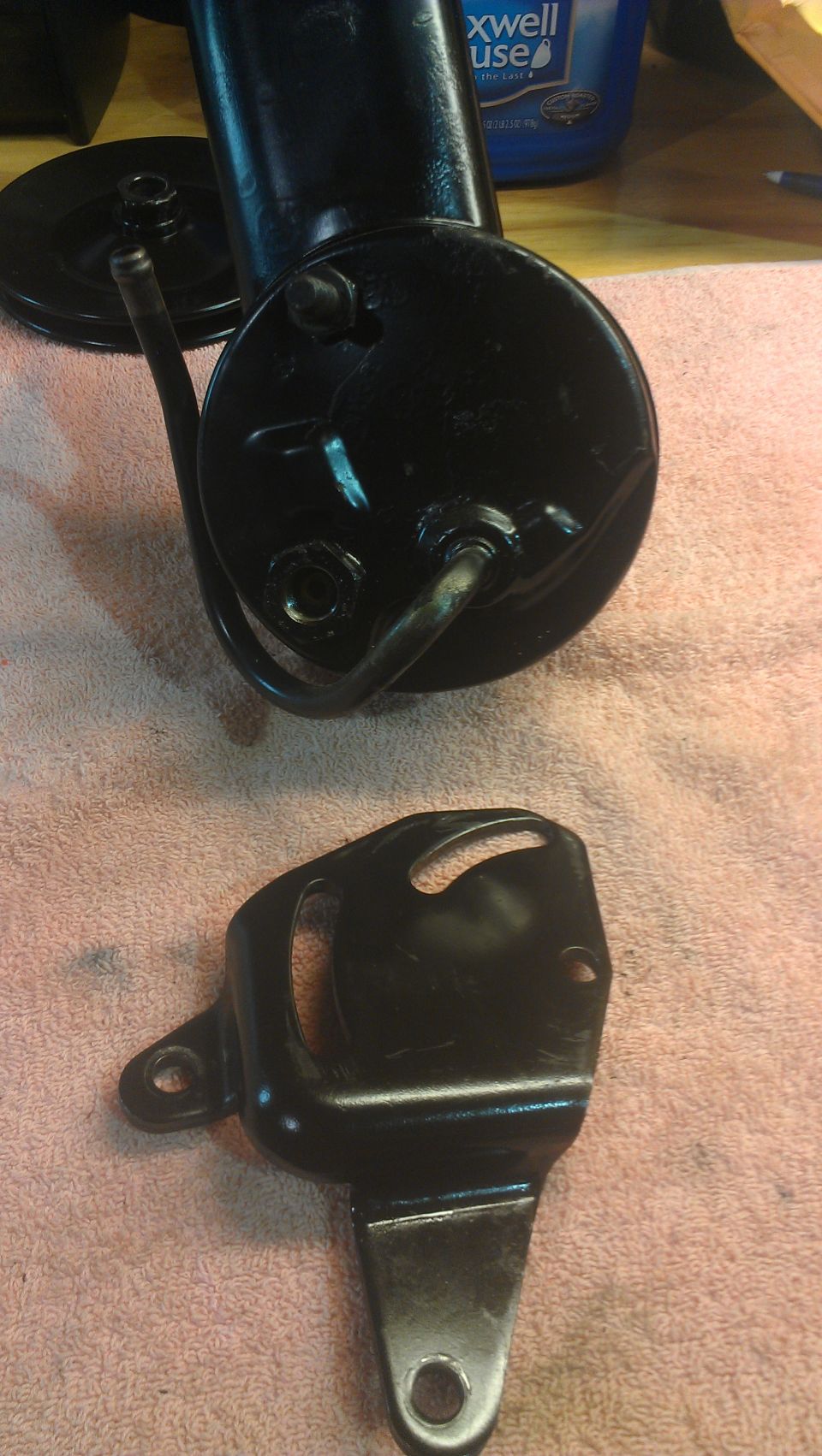 Black power steering pump with pulley and mounting bracket on a pink towel