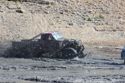 1978 Ford Bronco - A heavily mud-covered truck navigates a challenging off-road course, kicking up spray as it goes.