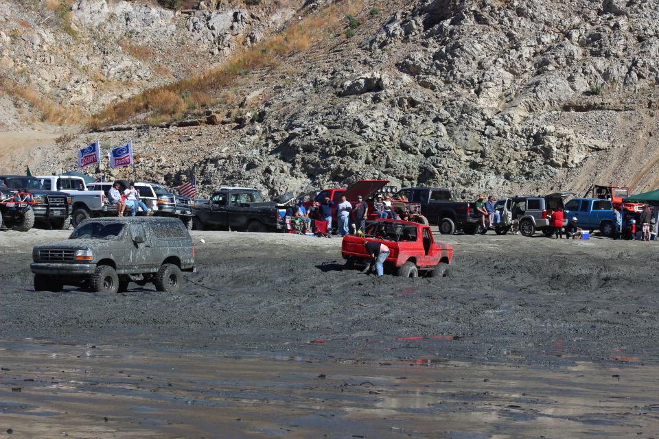 Mud bogging event with several off-road trucks and SUVs stuck in mud, with spectators watching