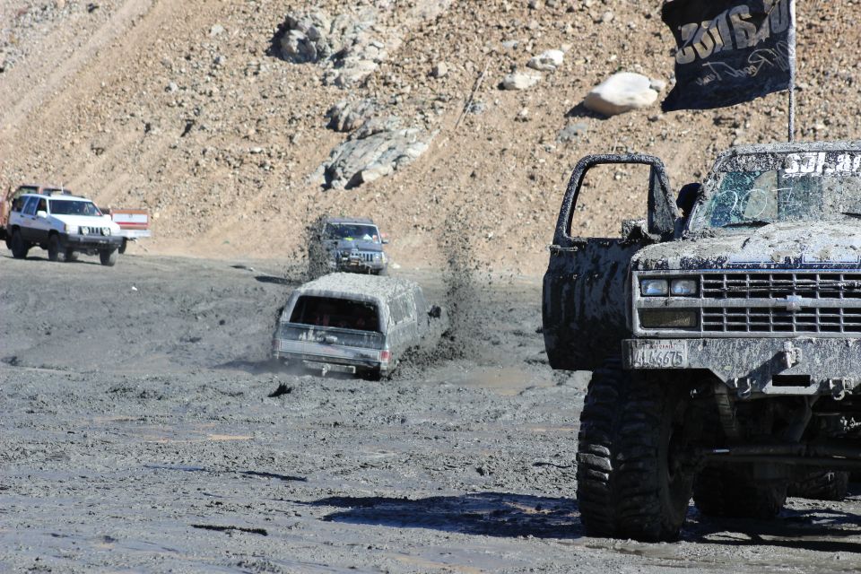 Muddy trucks and SUVs driving through a mire with a flag on one vehicle