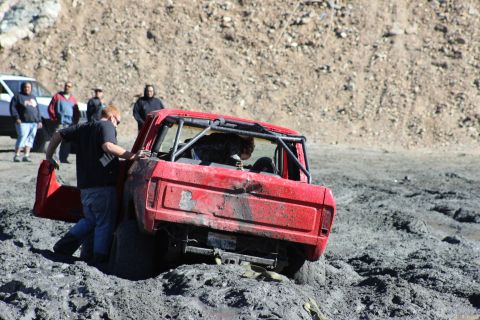 1978 Ford Bronco - A red 1978 Ford Bronco is stuck in thick mud, with people attempting to free it.